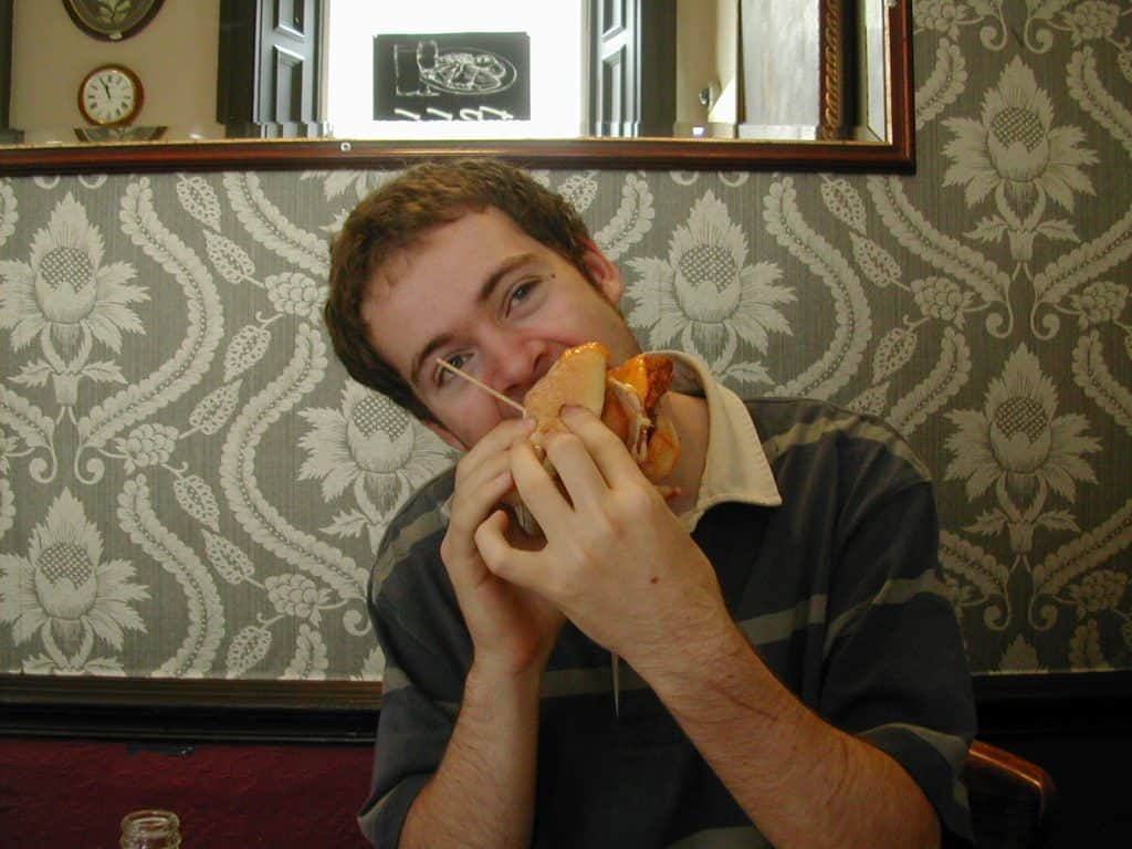 Man eating a large burger devoid of nutrition and goodness