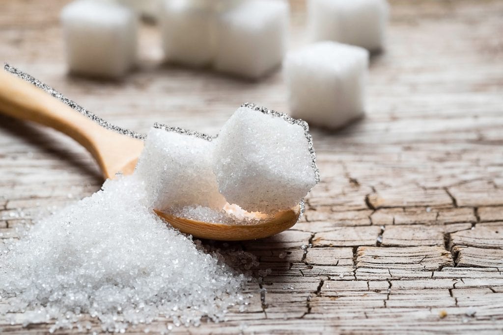 Lots of sugar, piled on a spoon, surrounded by sugar cubes in the background.